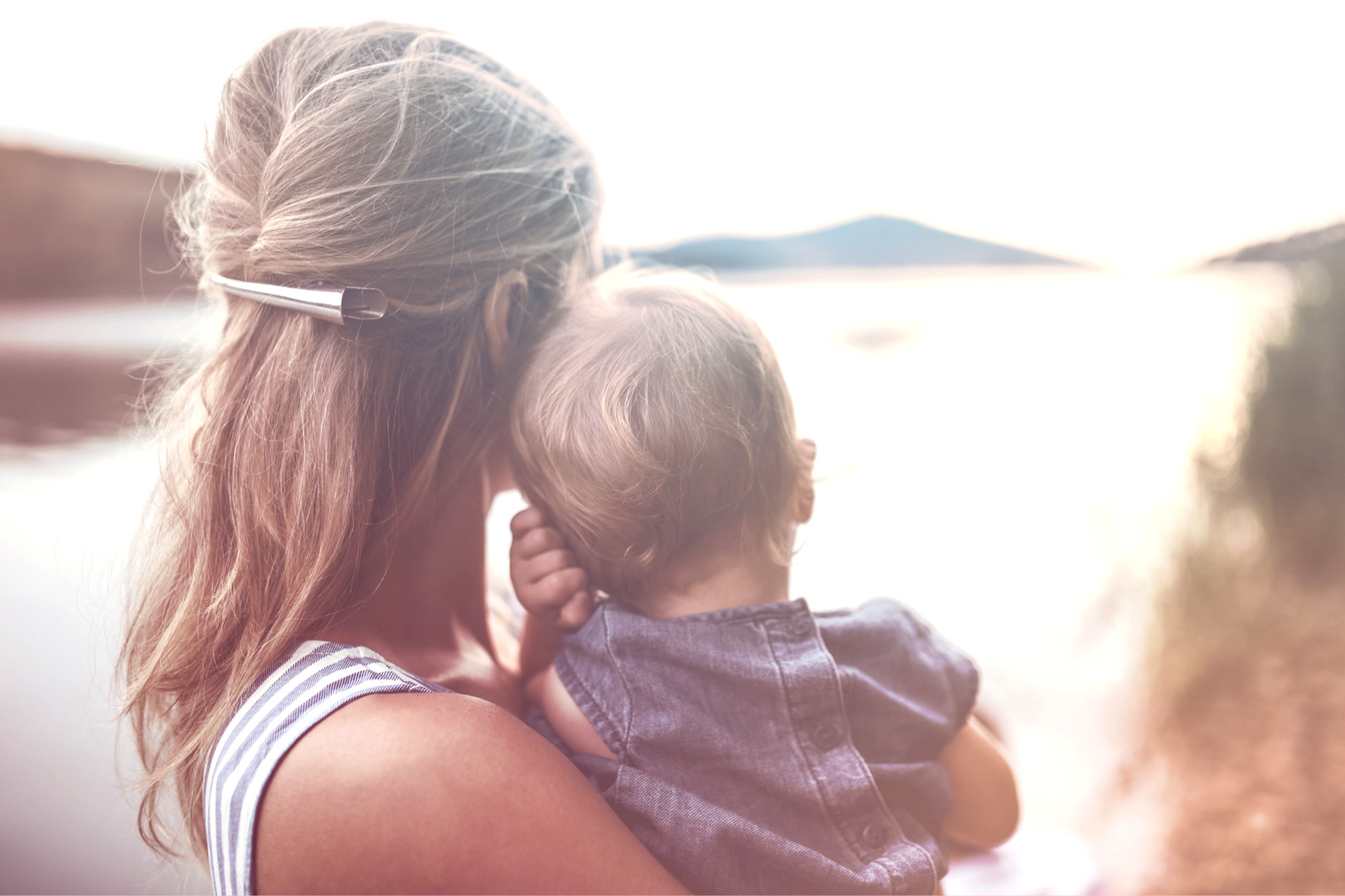 Una madre amorevole che guarda verso l'orizzonte mentre tiene in braccio un bambino piccolo, rappresentando la gioia di una famiglia che potrebbe essere stata aiutata da trattamenti di fertilità come la fertilizzazione intrauterina assistita.
