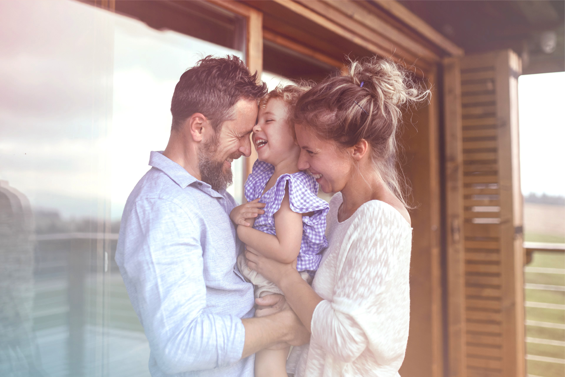 Famiglia felice a casa: una coppia sorridente che tiene in braccio un bambino piccolo, con una tenerezza evidente in un ambiente domestico luminoso, simboleggiando il successo di trattamenti come l'IUI.